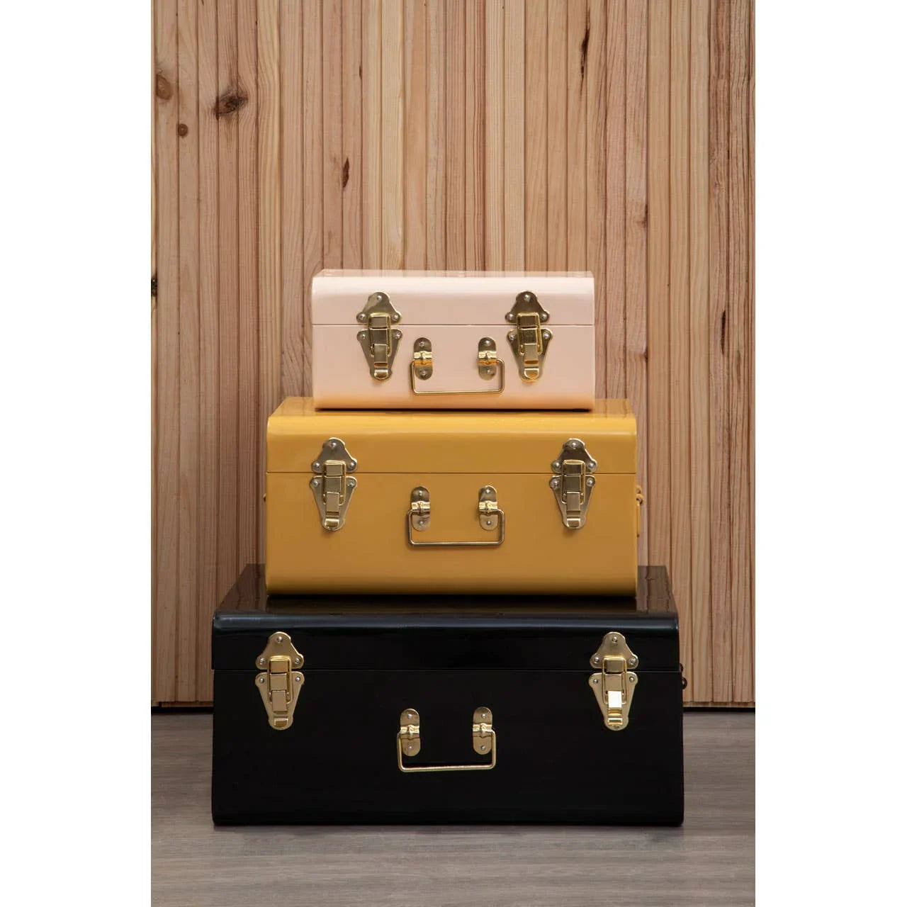 Set of three metal storage trunks in pink, yellow, and black with gold clasps on wood floor