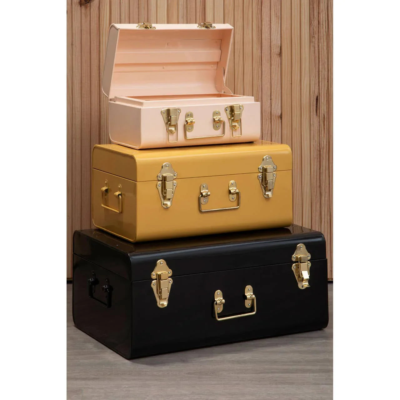 Stacked metal storage trunks in pink, yellow, and black with gold handles and clasps