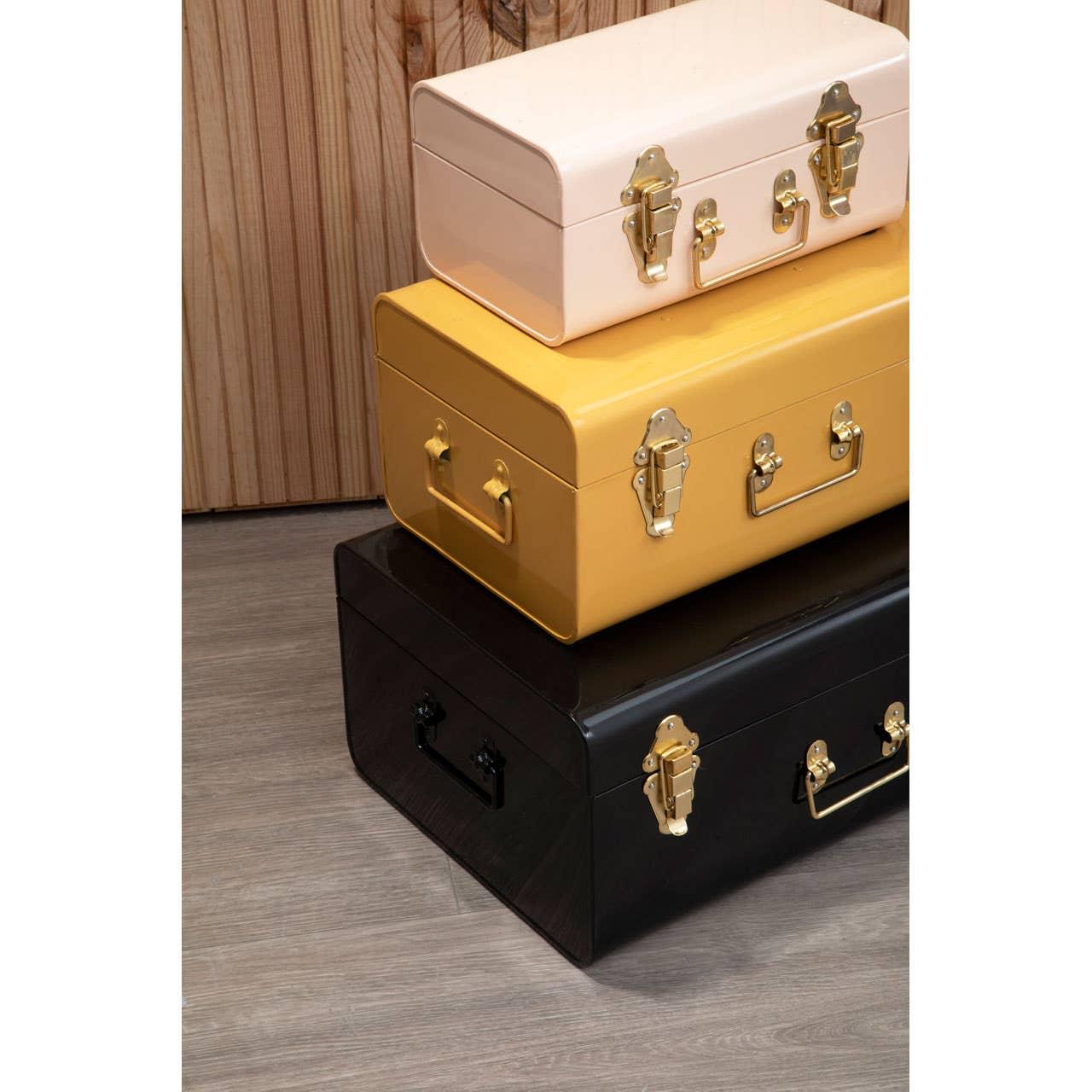 Stacked metal storage trunks in cream, yellow, and black with gold handles on wood floor