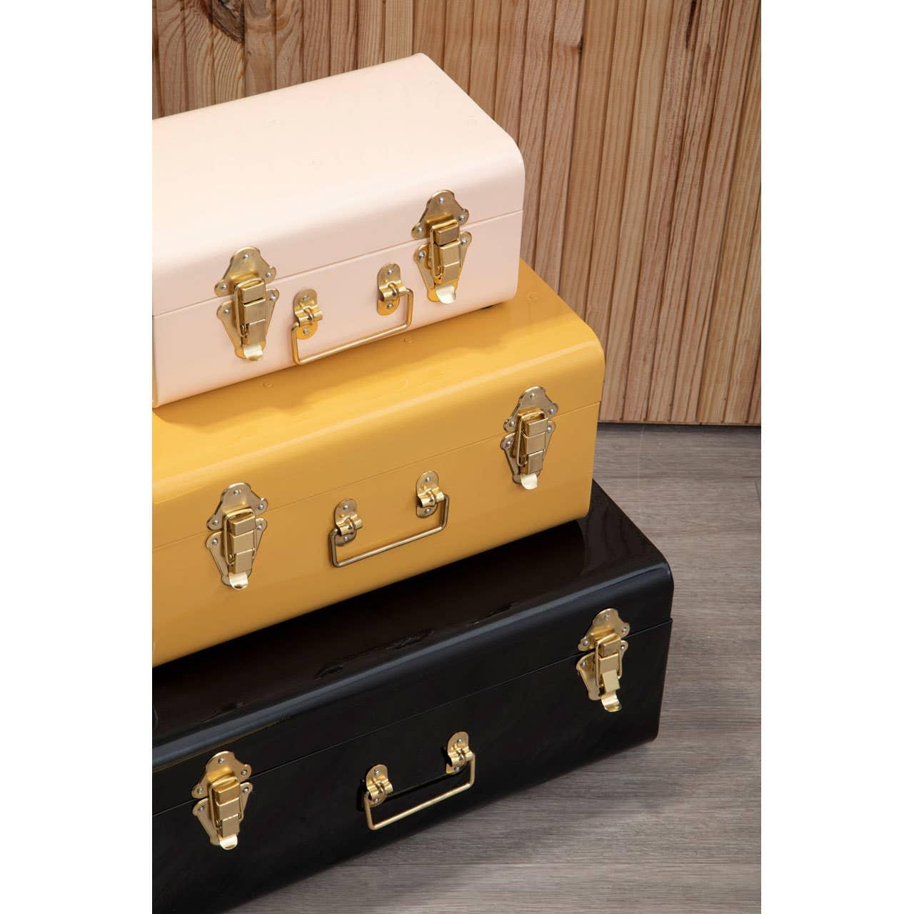 Stacked metal storage trunks in cream, yellow, and black with gold latches and handles