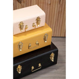 Stacked metal storage trunks in cream, yellow, and black with gold latches and handles