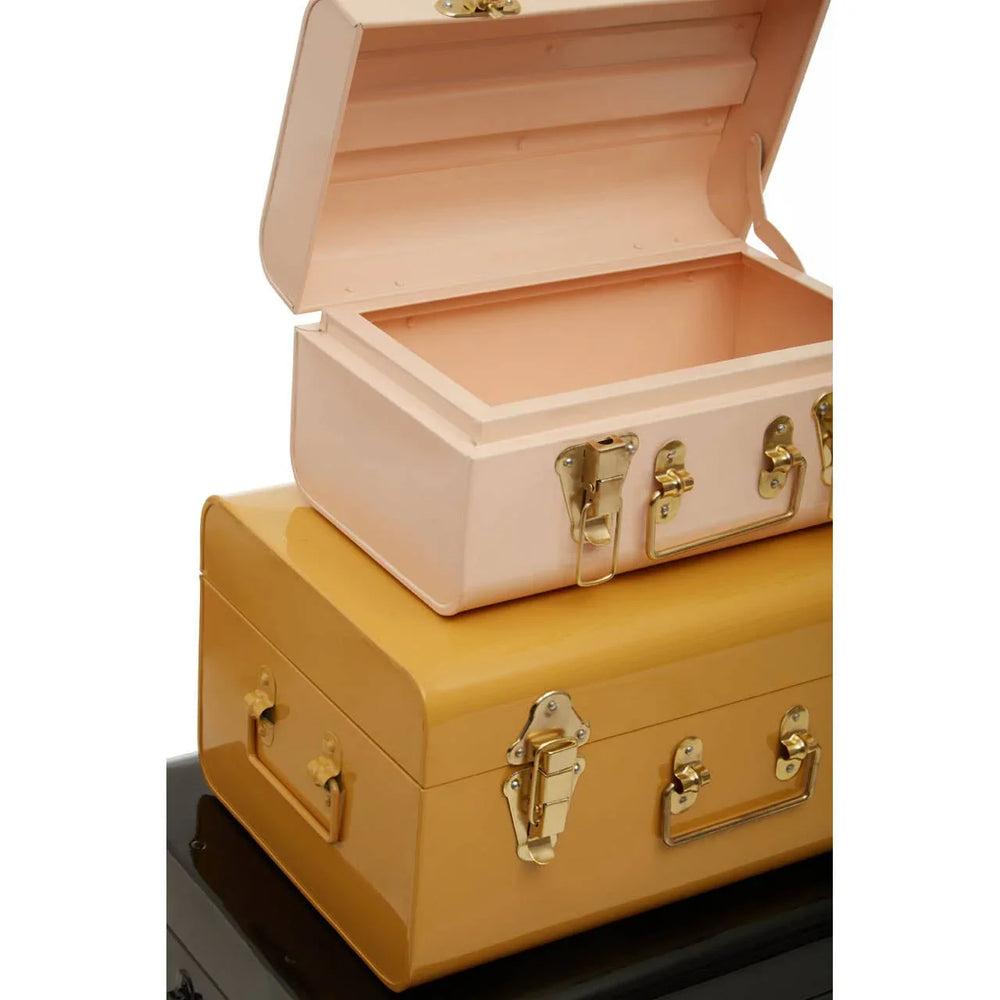 Stacked metal storage trunks in pink, yellow, and black with gold clasps and handles