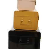 Stacked metal storage trunks in black, yellow, and beige with handle detail