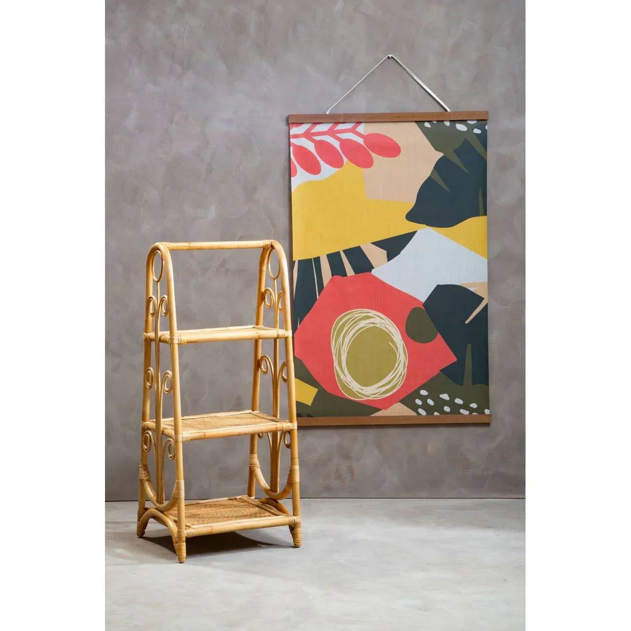 Three tier rattan shelving unit beside abstract wall art on a grey background