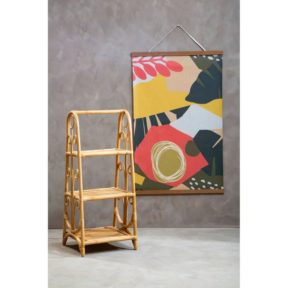 Three tier rattan shelving unit beside abstract wall art on a grey background