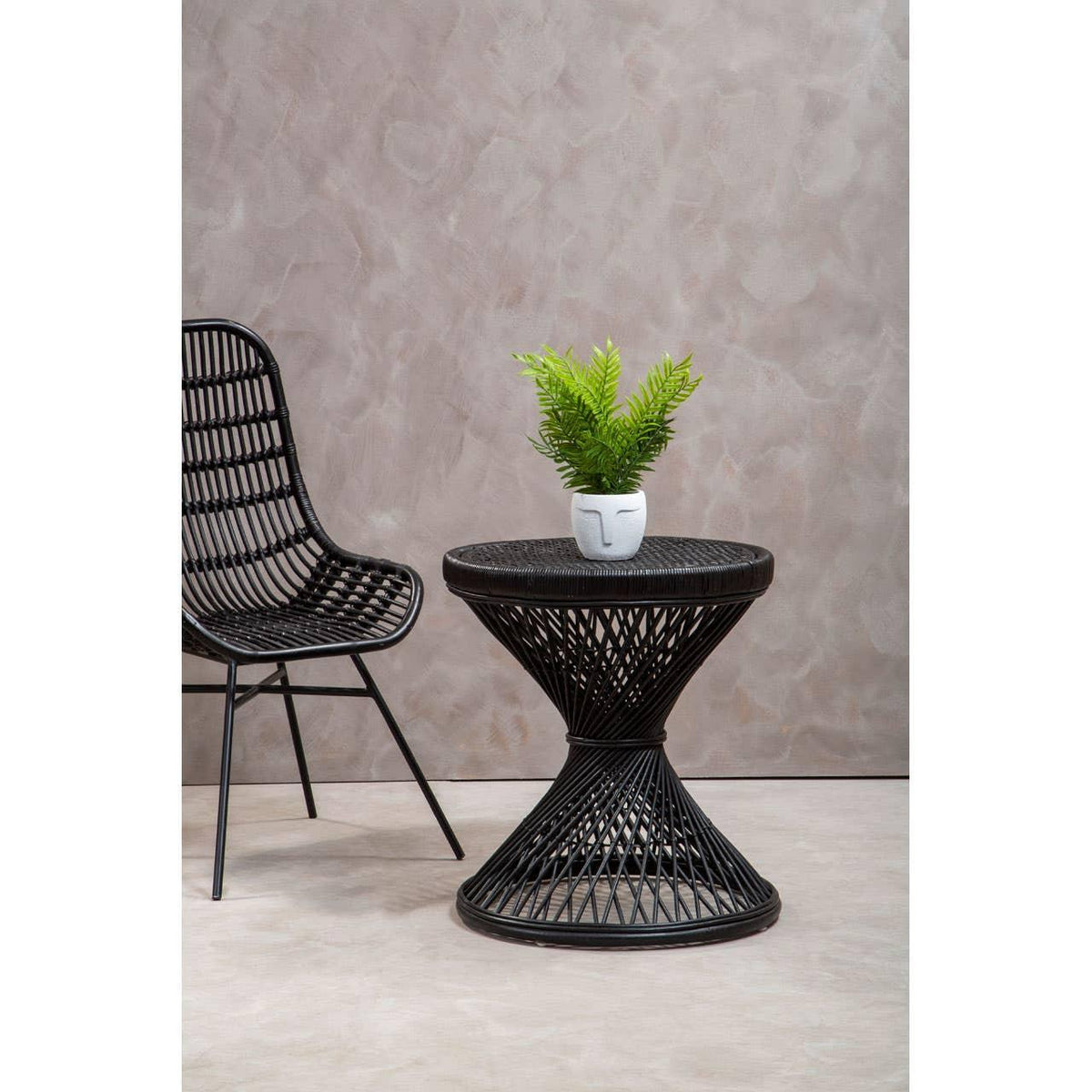 Black rattan accent chair and round wicker side table with plant in white vase