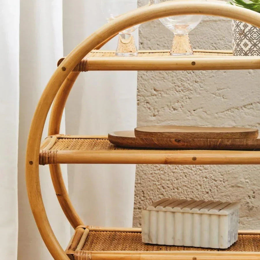 Round rattan shelving unit with glassware, decorative plant, and marble box on shelves
