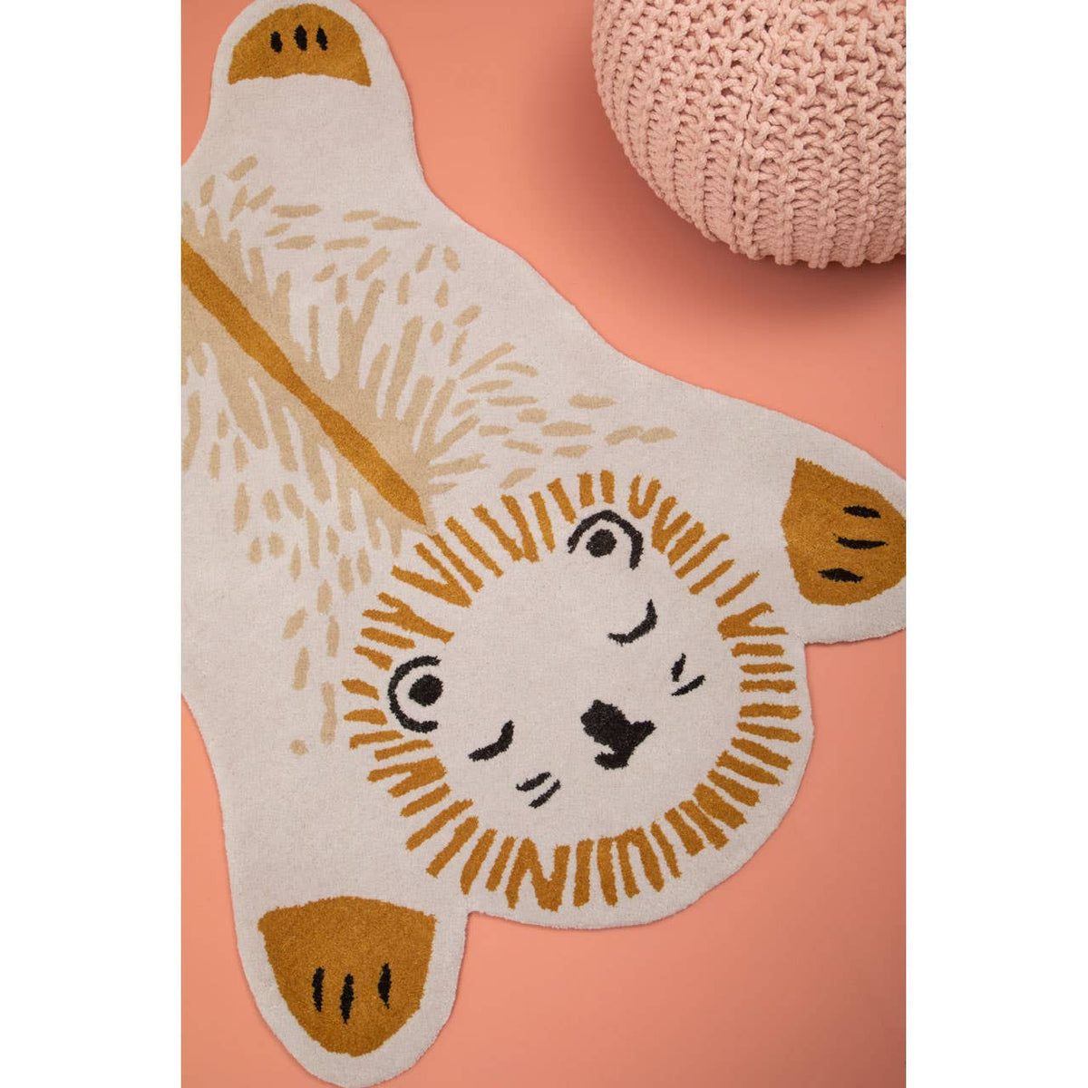 A soft pink pouffe designed for kids, featuring a textured surface and a round shape, placed on a light pink background alongside a playful lion-shaped rug with a white and gold design