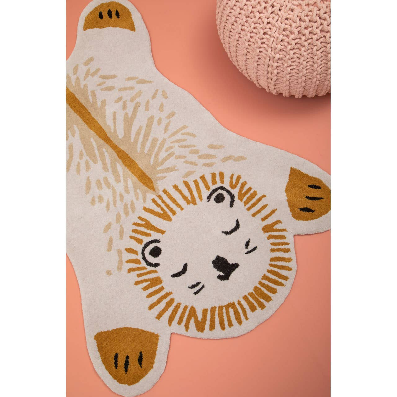 A soft pink pouffe designed for kids, featuring a textured surface and a round shape, placed on a light pink background alongside a playful lion-shaped rug with a white and gold design