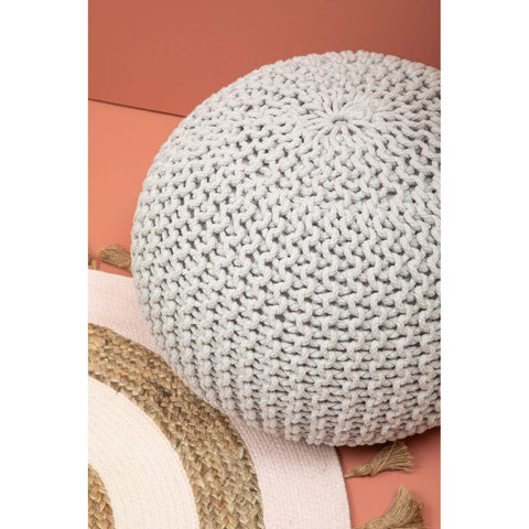 A round grey knit pouffe resting on a textured pink and beige surface, showcasing its intricate knitted pattern and soft, cozy appearance