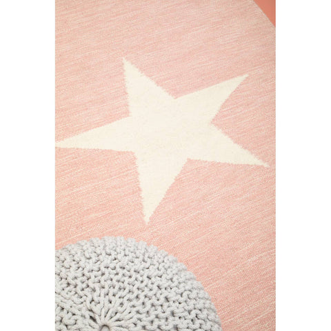 A soft grey knit pouffe designed for kids, featuring a textured surface and a cozy appearance, placed on a light pink rug with a large cream star and a circular grey pattern