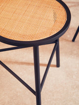 Round rattan seat stool featuring a natural woven top and sleek black metal legs, showcasing a modern design with a minimalist aesthetic. The stool is positioned on a light-colored floor, highlighting its texture and structure