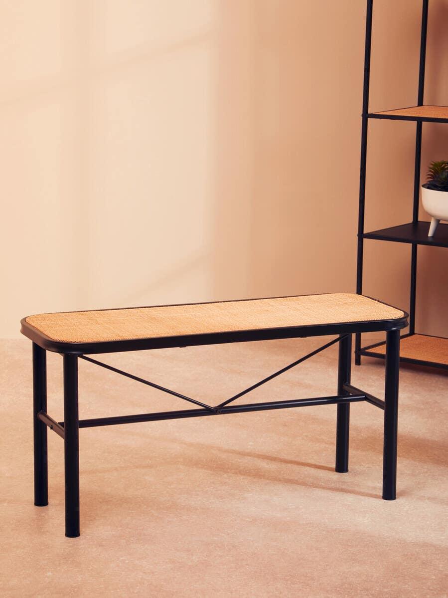 Black metal bench with woven rattan seat on beige floor near shelving unit