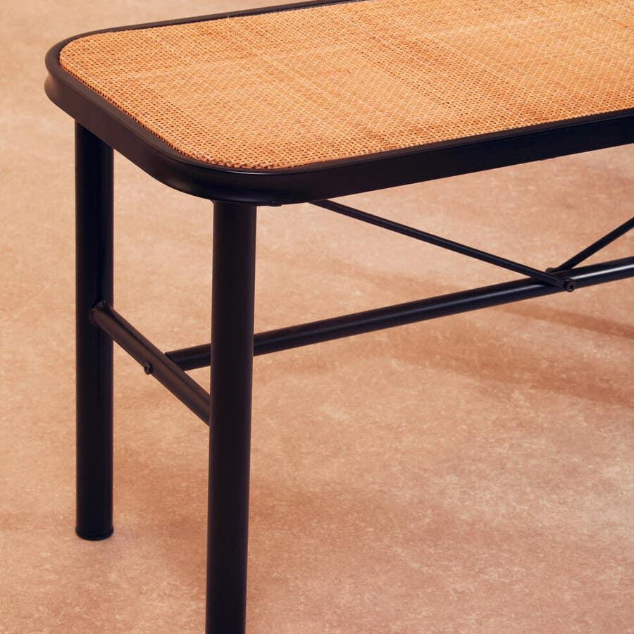 Closeup of rattan bench seat with black metal frame and legs on beige floor