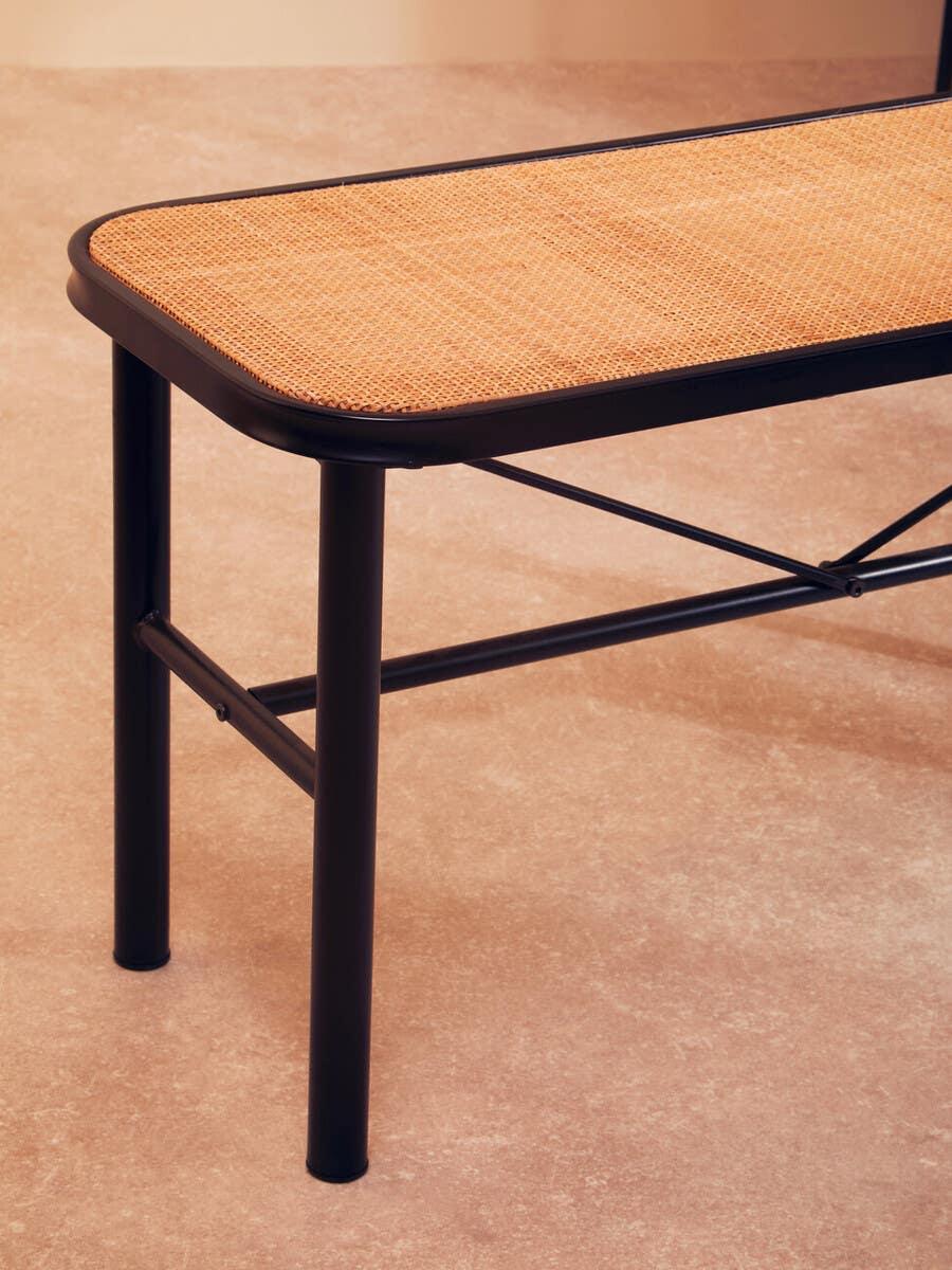 Closeup of rattan bench seat with black metal frame and legs on beige floor