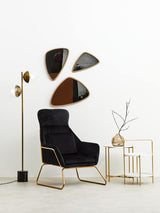 A stylish two-tier side table featuring a white top and gold metal frame, positioned next to a black upholstered armchair. The table is complemented by decorative elements, including a slender vase with branches and modern wall mirrors in abstract shapes above. A floor lamp with a gold finish stands nearby, enhancing the contemporary aesthetic of the space