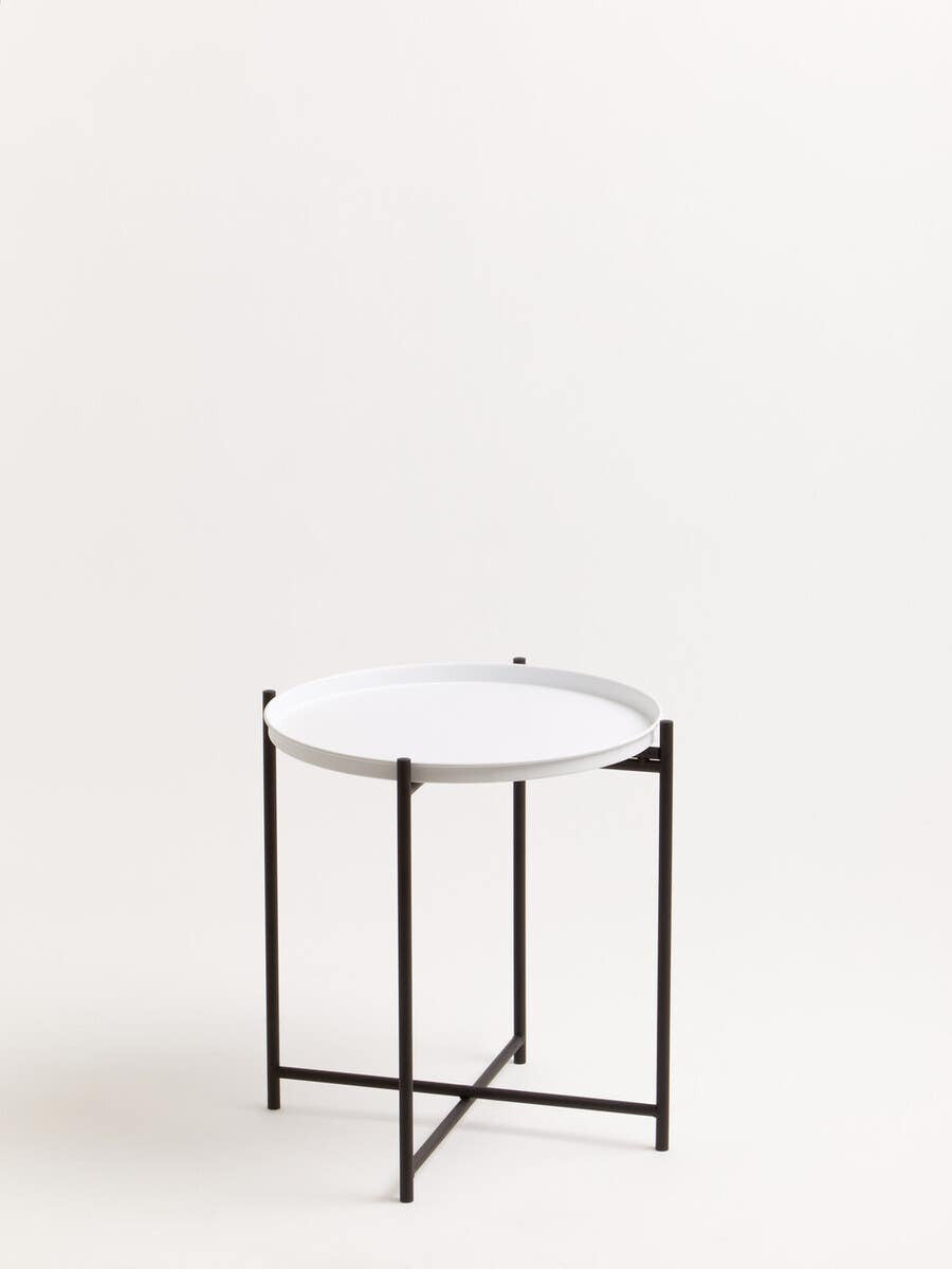 Round white tabletop supported by a sleek black metal frame, featuring a minimalist design with four legs and a crossbar for stability. The background is a neutral color, enhancing the modern aesthetic of the side table