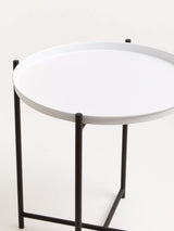 Round white tabletop supported by a sleek black metal frame, featuring four slender legs. The design is modern and minimalistic, suitable for various home decor styles
