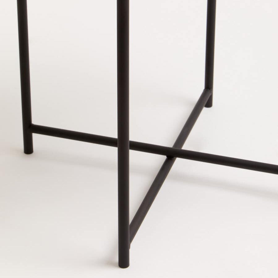 Round white tabletop supported by a sleek black metal frame with a crossbar design, showcasing a modern and minimalist aesthetic. The table's legs are slender and angular, creating a stylish contrast with the smooth surface