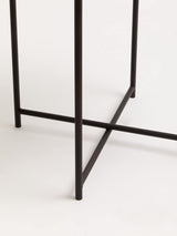 Round white tabletop supported by a sleek black metal frame with a crossbar design, showcasing a modern and minimalist aesthetic. The table's legs are slender and angular, creating a stylish contrast with the smooth surface