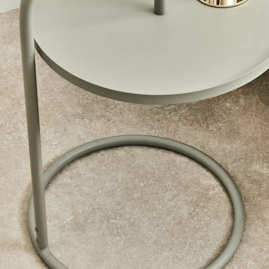 Grey hanging top side table with a circular base and a sleek, minimalist design. The tabletop is round and smooth, supported by a slender metal frame that features a unique hanging structure. The table is placed on a light-colored surface, highlighting its modern aesthetic