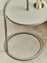 Grey hanging top side table with a circular base and a sleek, minimalist design. The tabletop is round and smooth, supported by a slender metal frame that features a unique hanging structure. The table is placed on a light-colored surface, highlighting its modern aesthetic