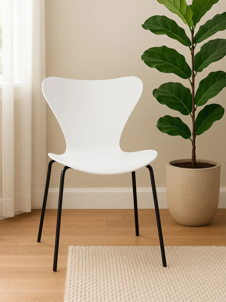 White modern dining chair with black metal legs on wooden floor beside large potted plant