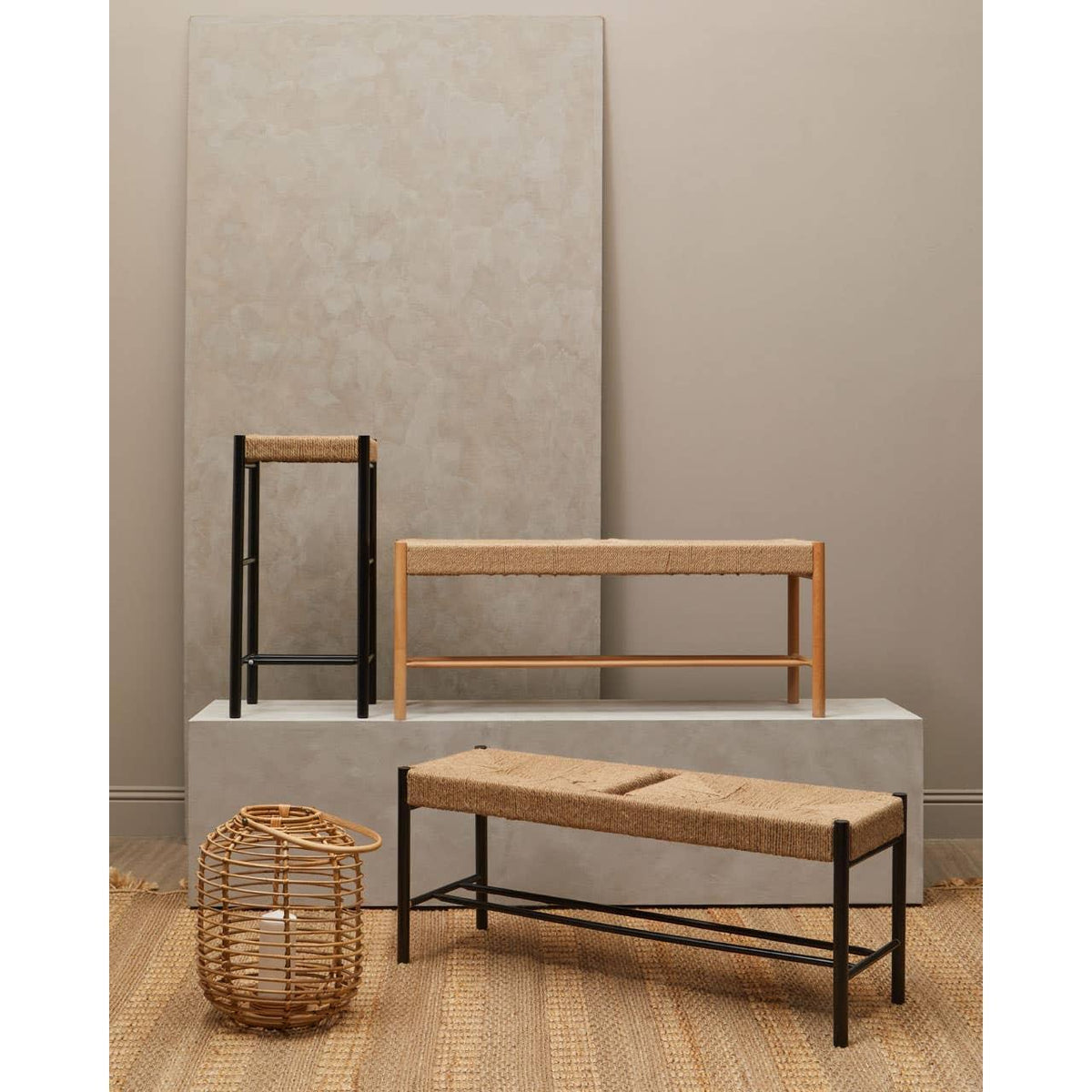 Seagrass bench and stools with black and natural wood frames on woven rug in neutral room