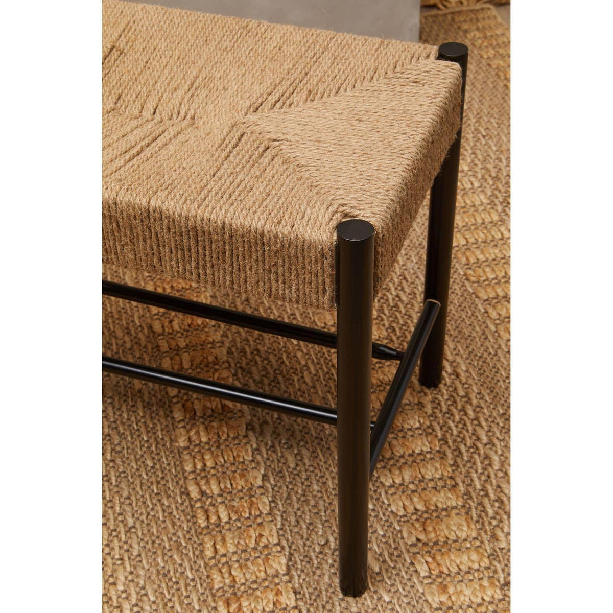 Woven seat bench with black metal legs on textured jute rug