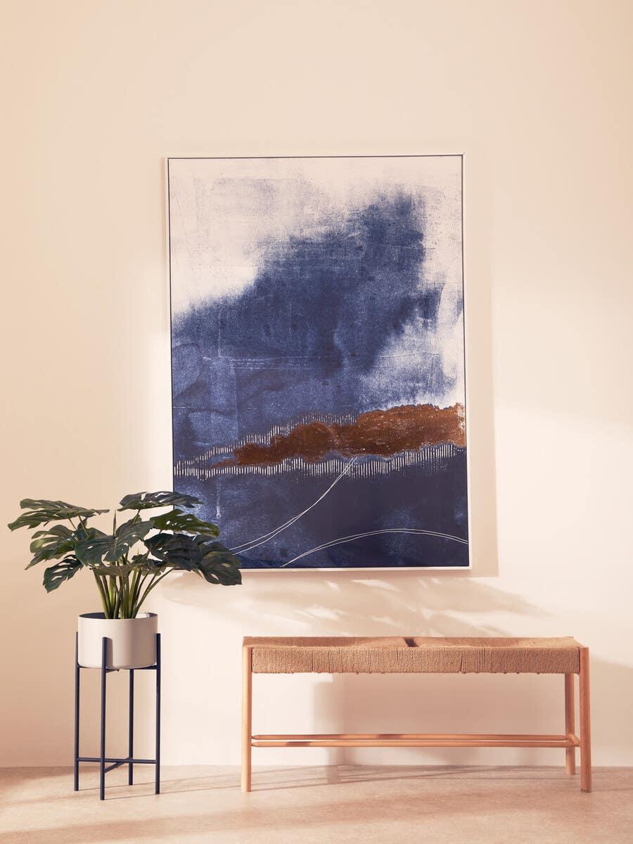 Natural wood woven bench beside potted plant and large abstract wall art in hallway
