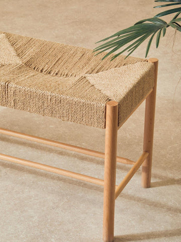 Natural woven bench with light wood frame on beige floor, decorative plant in view