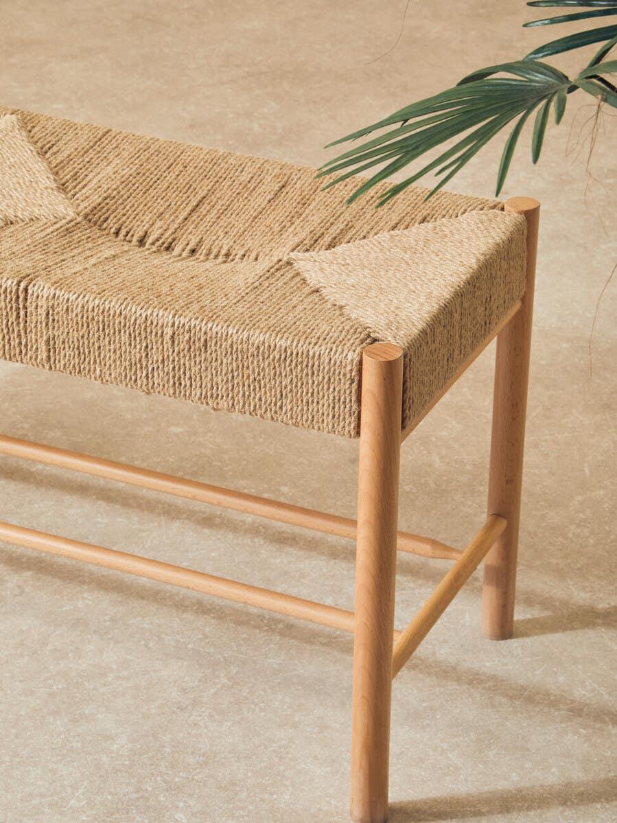 Natural woven bench with light wood frame on beige floor, decorative plant in view