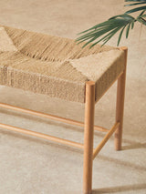 Natural woven bench with light wood frame on beige floor, decorative plant in view