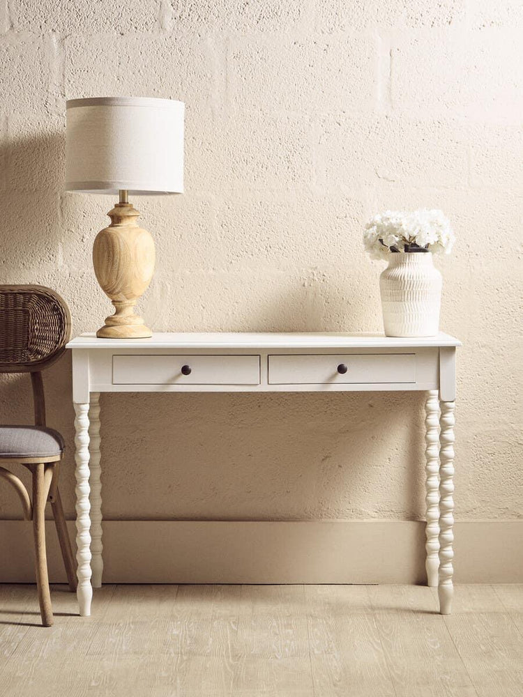 White console table with two drawers, spiral legs, lamp, and vase against beige wall