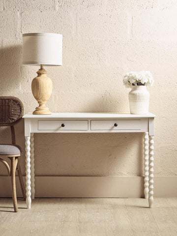 White console table with two drawers, spiral legs, lamp, and vase against beige wall