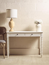 White console table with two drawers, spiral legs, lamp, and vase against beige wall