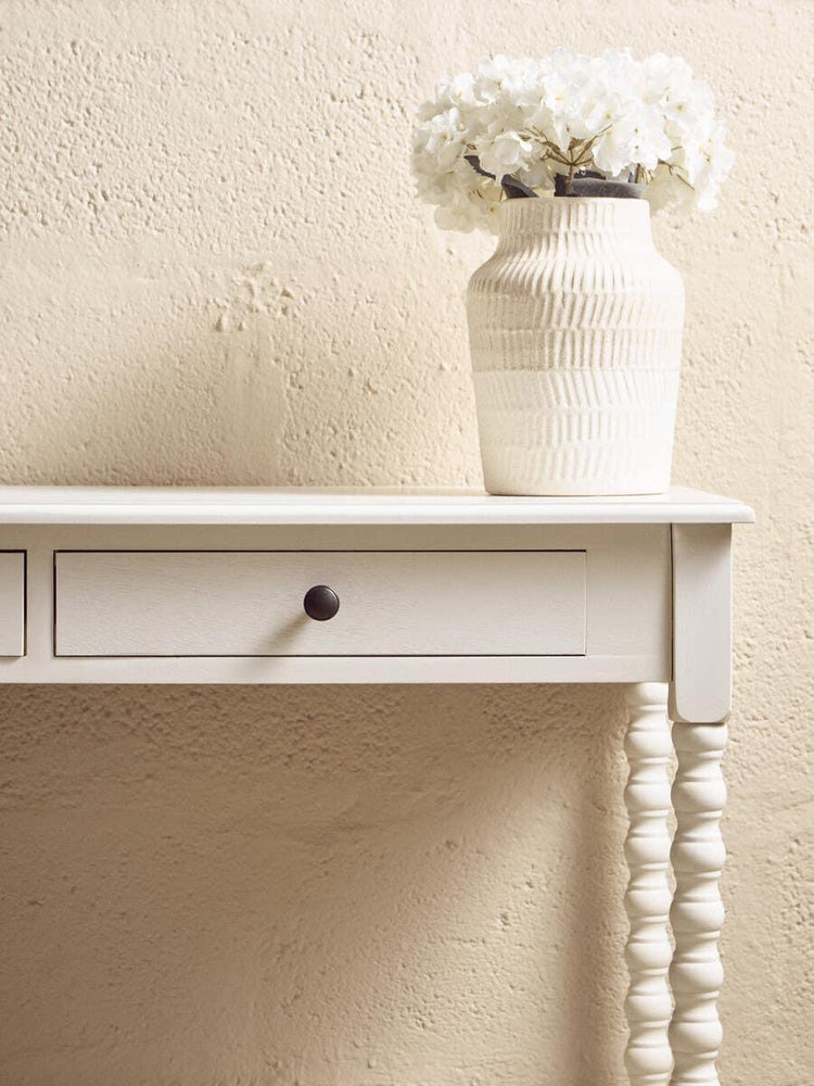 White console table with spindle leg, single drawer and cream ceramic vase with white flowers