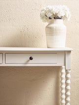 White console table with spindle leg, single drawer and cream ceramic vase with white flowers