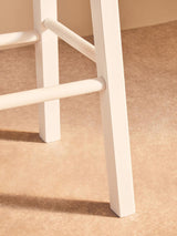 Close view of cream wooden chair leg and rungs on neutral carpeted floor