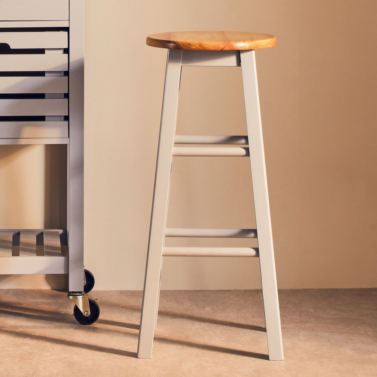 Natural wood seat with a light grey wooden frame, featuring four legs and a simple design, positioned next to a metal cart in a softly lit room