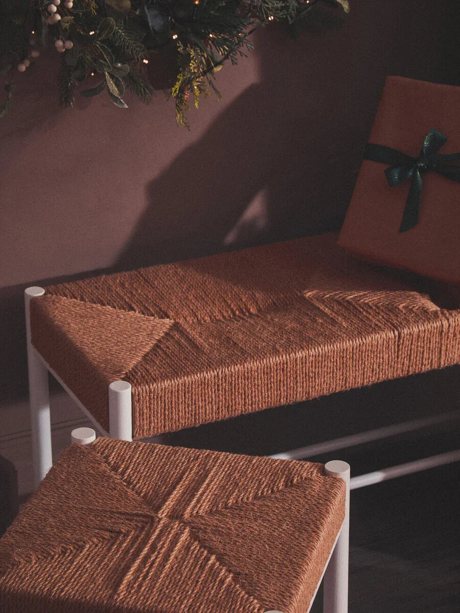 Brown woven bench and matching stool with white metal legs, set in a festive room