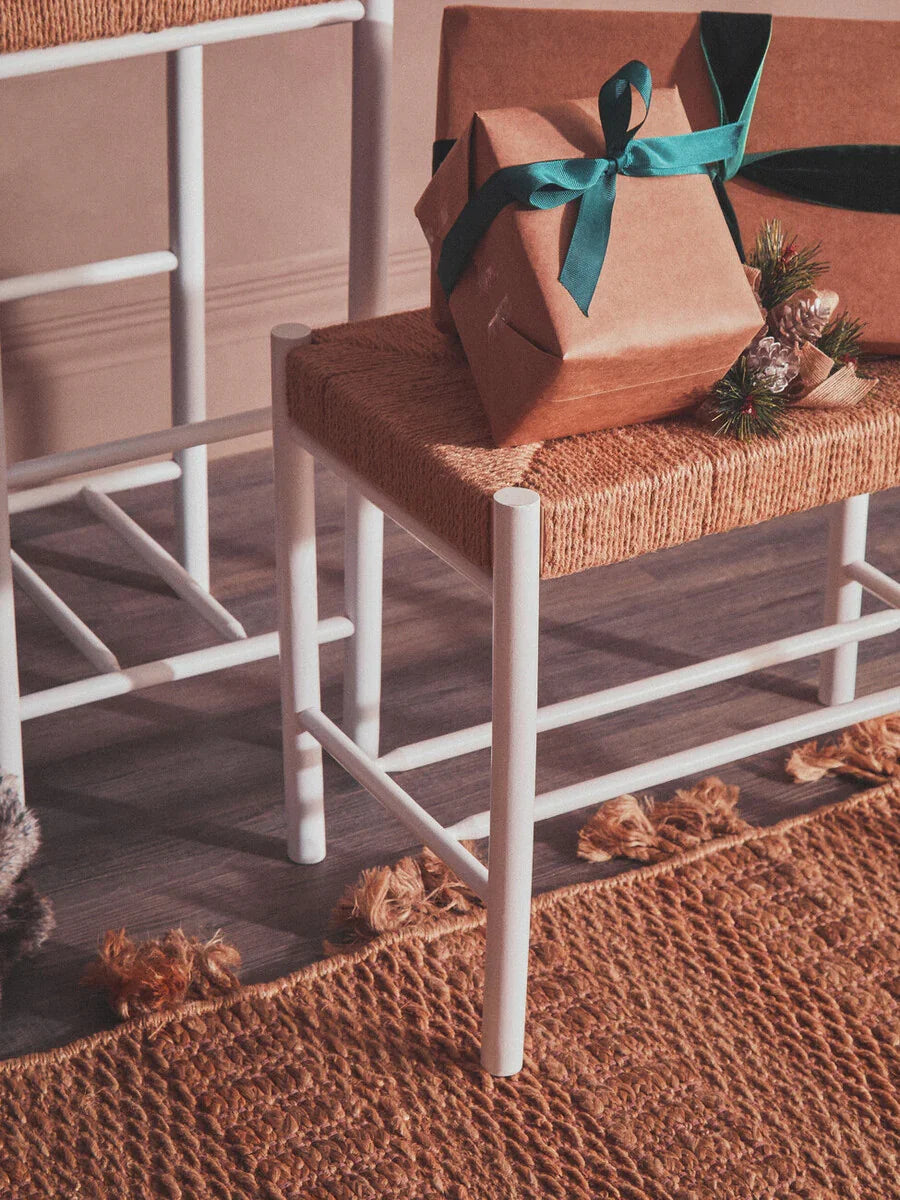 White bar stool with woven seat and gift box on natural jute rug