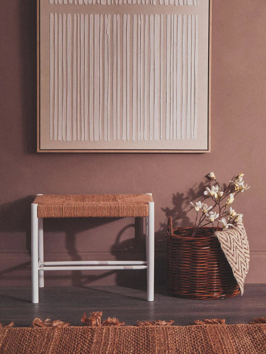 Woven seat wooden bench with white frame beside wicker basket and neutral wall art