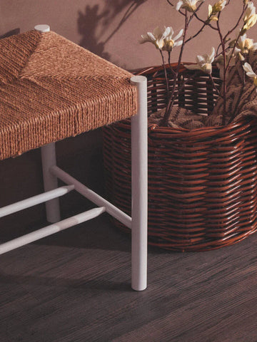 Woven seat stool with white legs beside brown wicker basket and artificial flowers