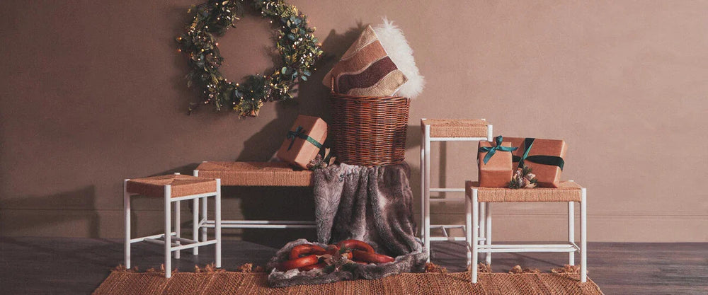 Wicker storage basket with cushion, woven stools, wrapped gifts, and holiday wreath