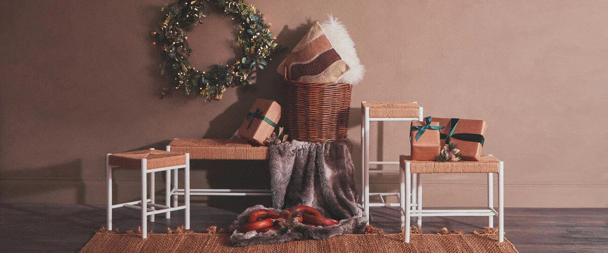 Wicker storage basket with cushion, woven stools, wrapped gifts, and holiday wreath