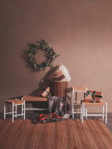 Woven rattan bench and stools with white frames on jute rug, gifts and wicker basket displayed