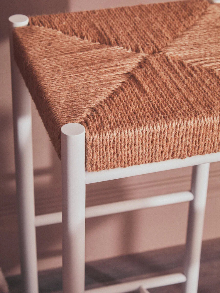 Close-up of woven seagrass bar stool seat with white metal legs against blush wall