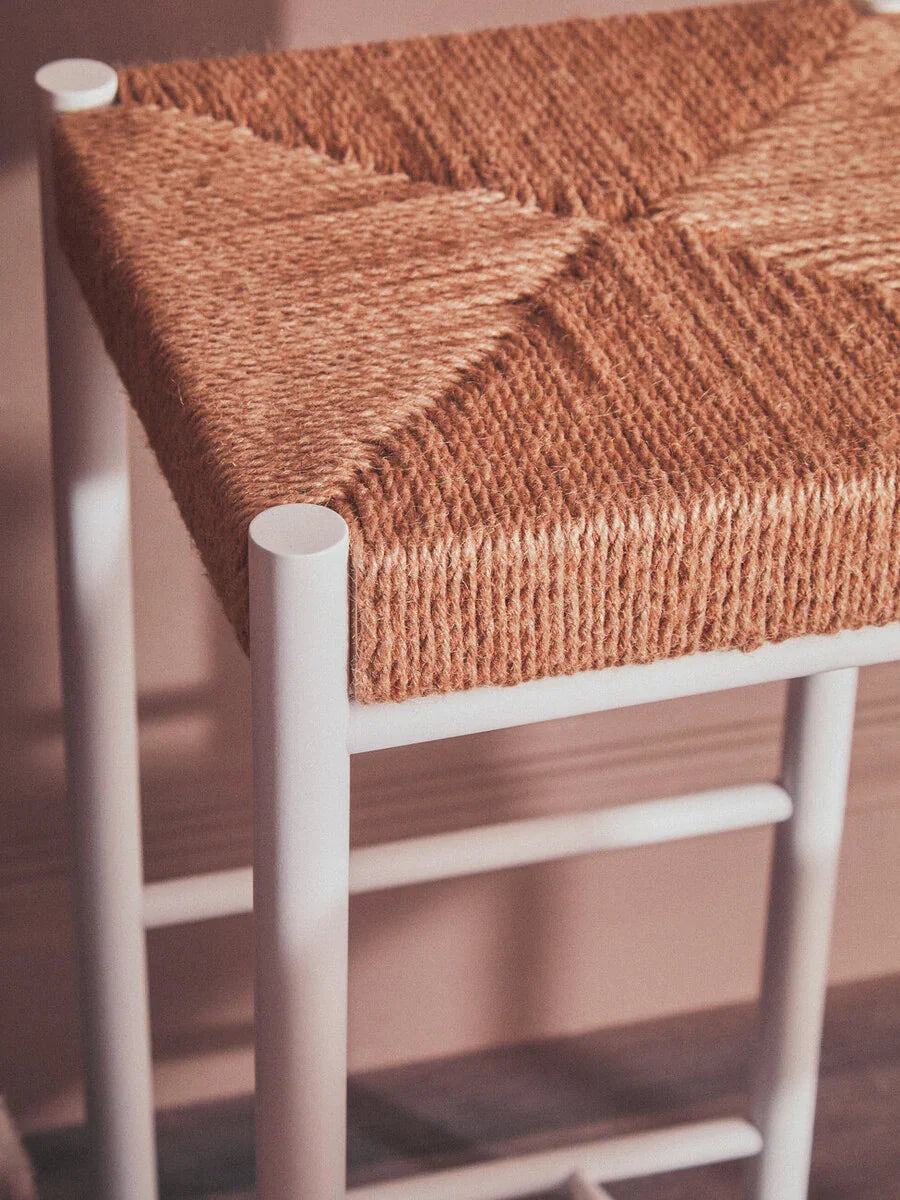 Close-up of woven seagrass bar stool seat with white metal legs against blush wall