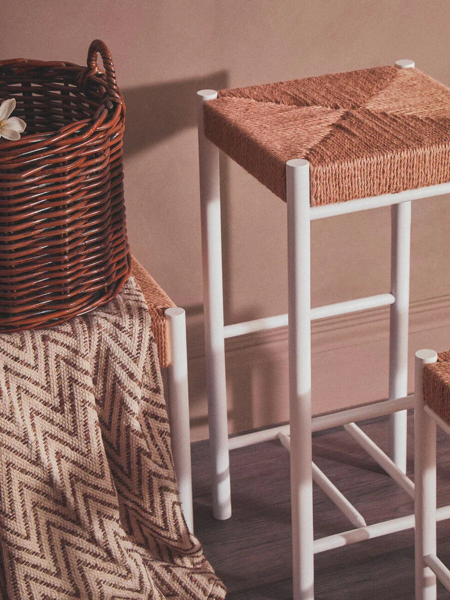 White bar stool with woven rattan seat beside brown wicker basket and chevron throw blanket
